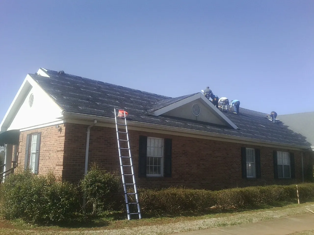 Crew tearing shingles off a brick ranch roof with a ladder set — Metal Roof Repair work by our crew in Glendale