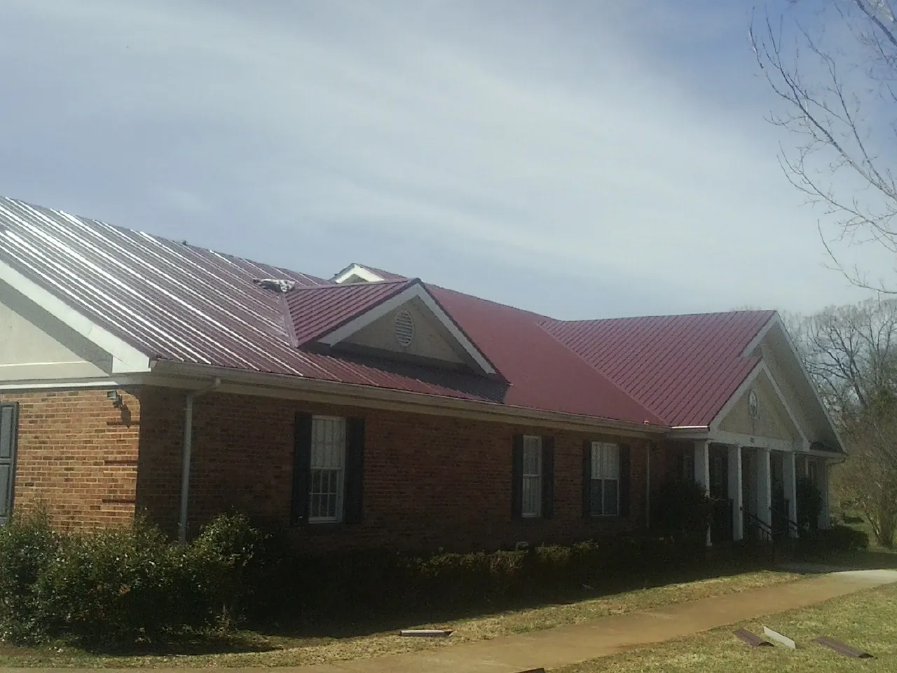 Red metal roof with gabled entries on a long brick building, from a Hail Damage Roof Repair job in Glendale