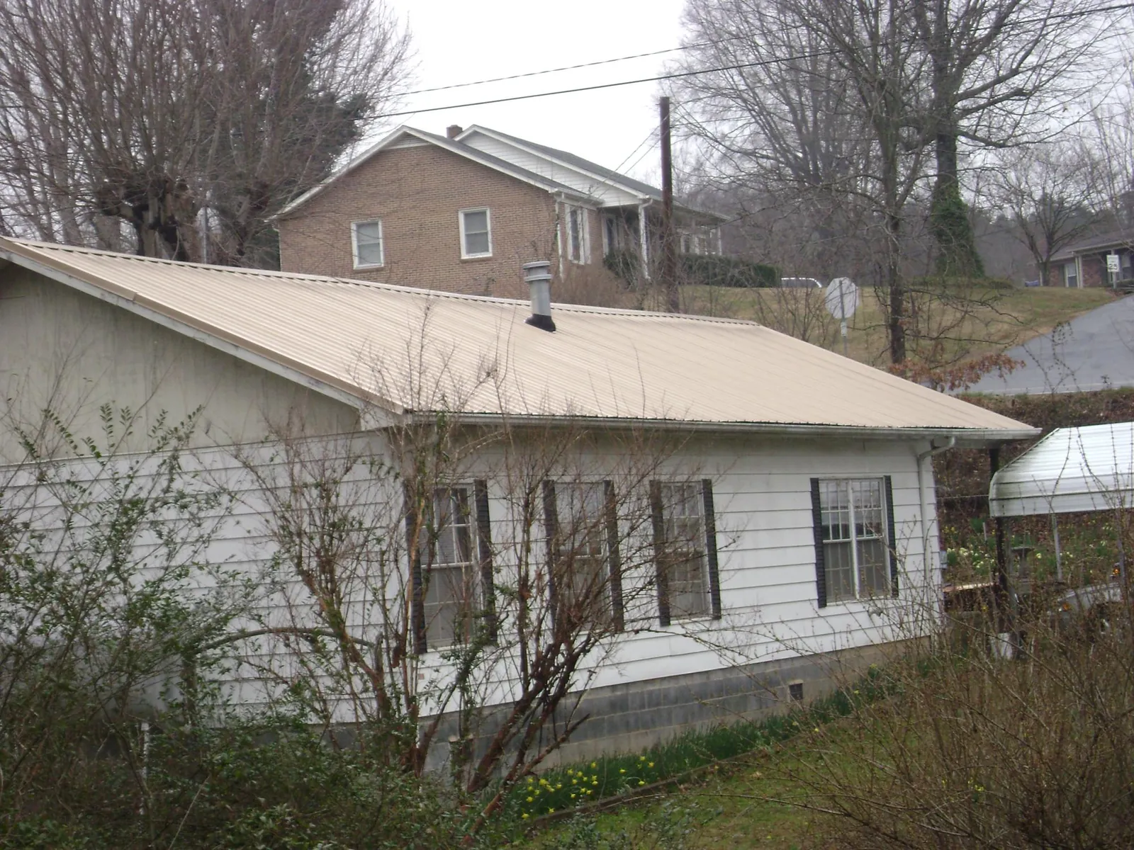 Tan metal roof on a white sided house set into a hillside — Commercial Roofing by Roofing Brothers in Glendale